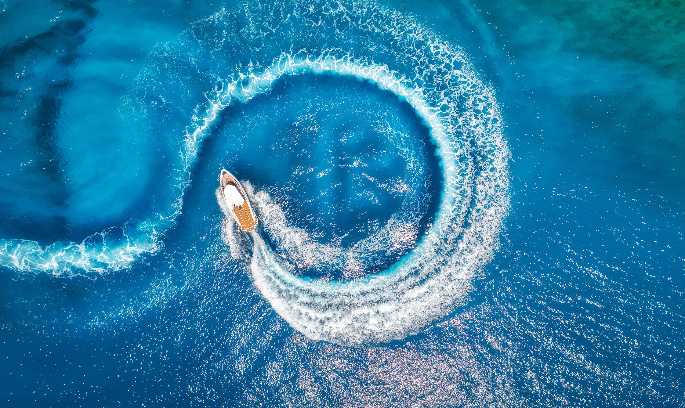 Aerial view of a motor boat carving a circular wake across clear blue water