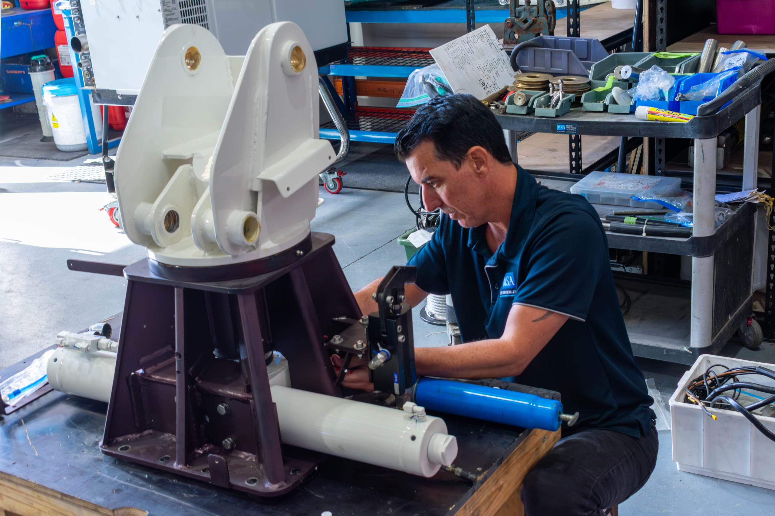 Technician fitting hydraulic cylinders to a davit crane slewing pedestal in the workshop