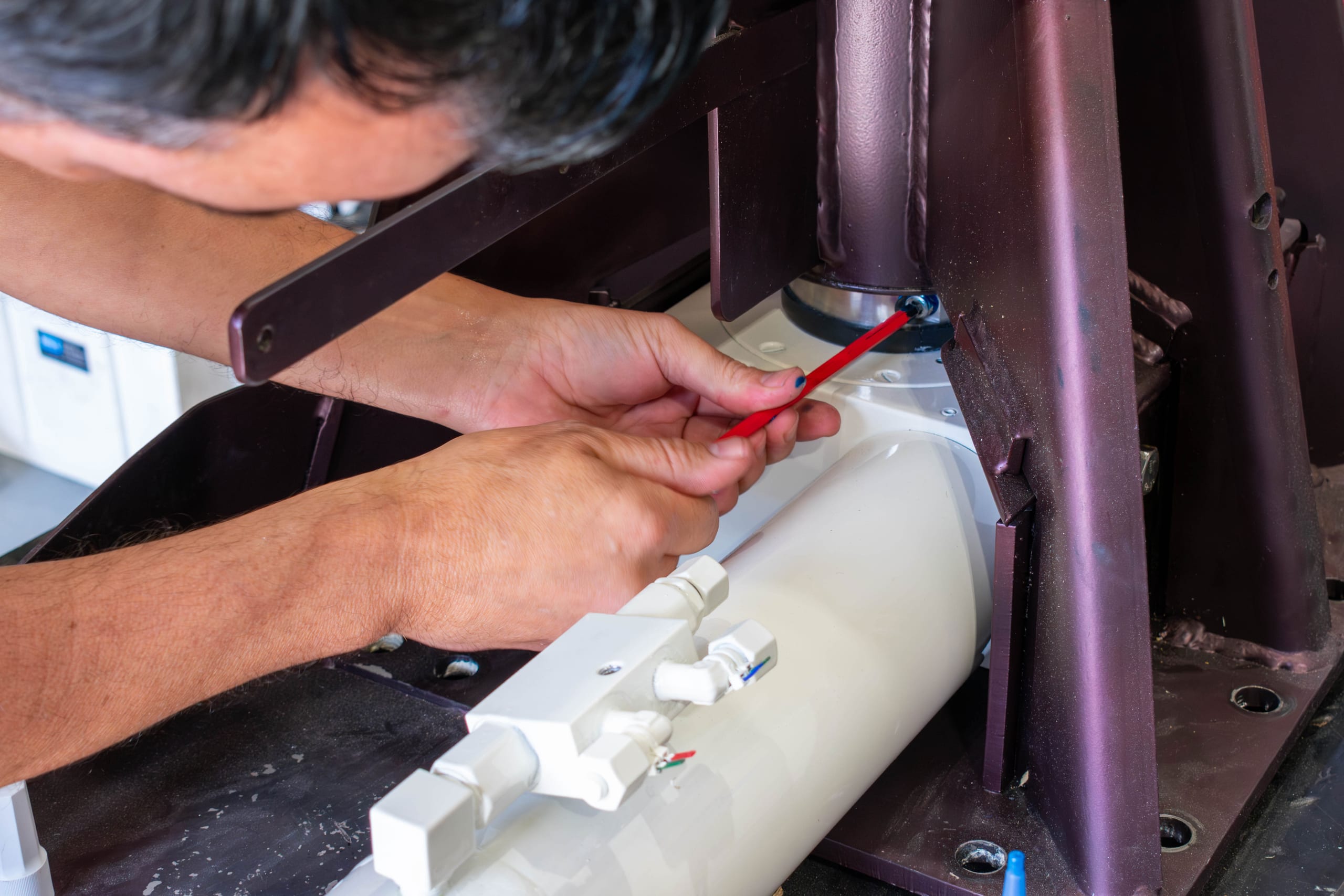 Technician checking hydraulic cylinder fittings on a davit crane pedestal during reassembly