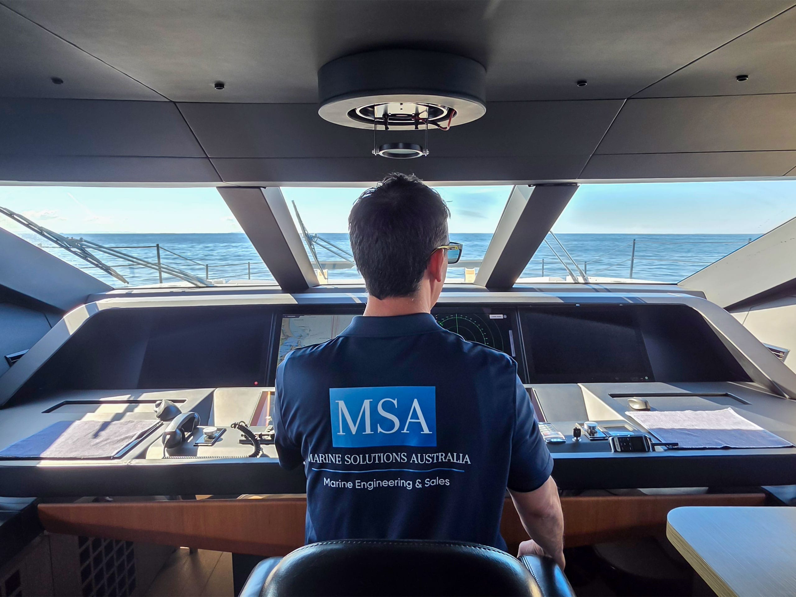 Marine Solutions delivery skipper at the helm of a motor yacht underway, chartplotter and radar in use