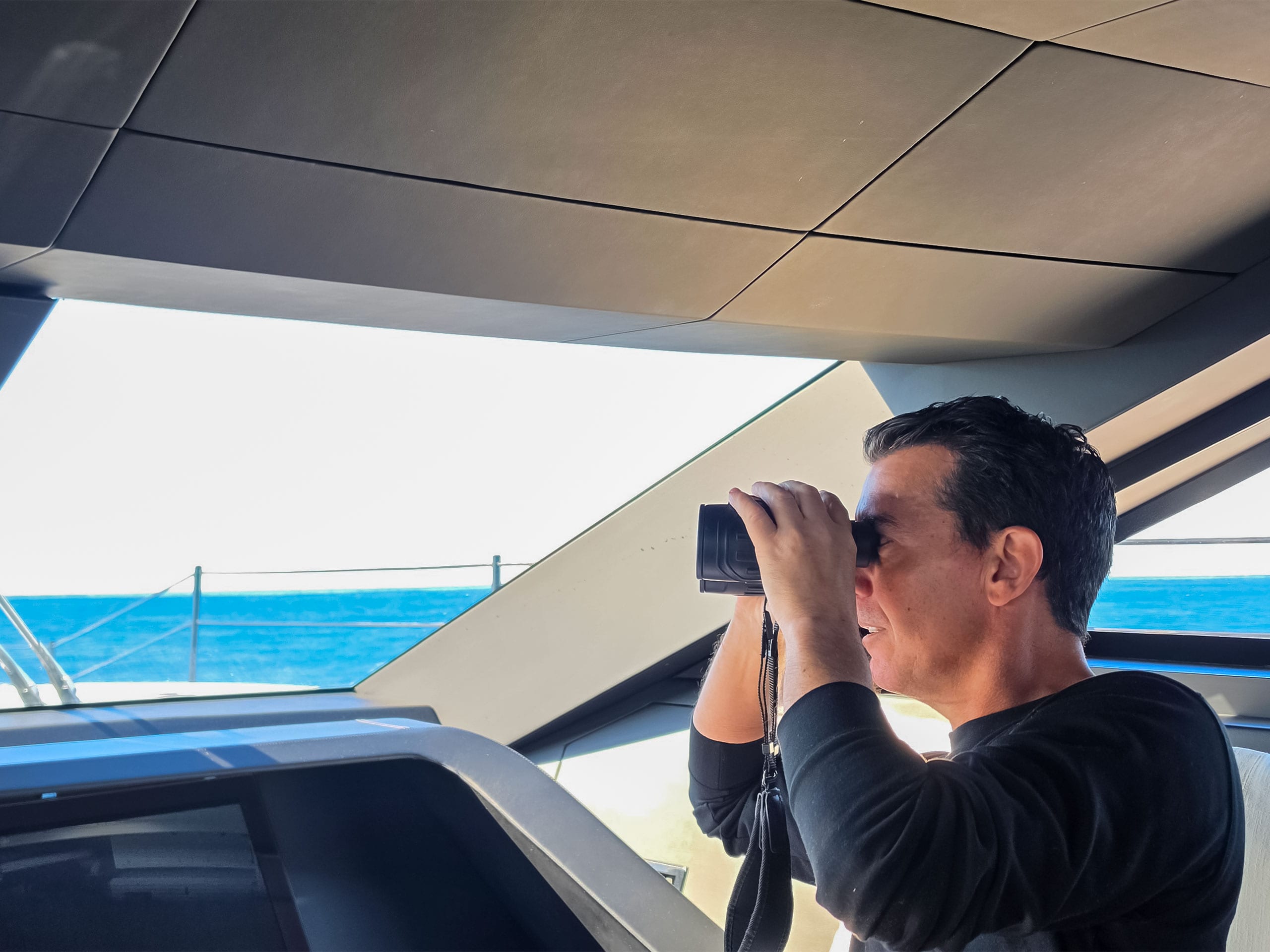 Crew member keeping lookout with binoculars from the bridge during a delivery passage
