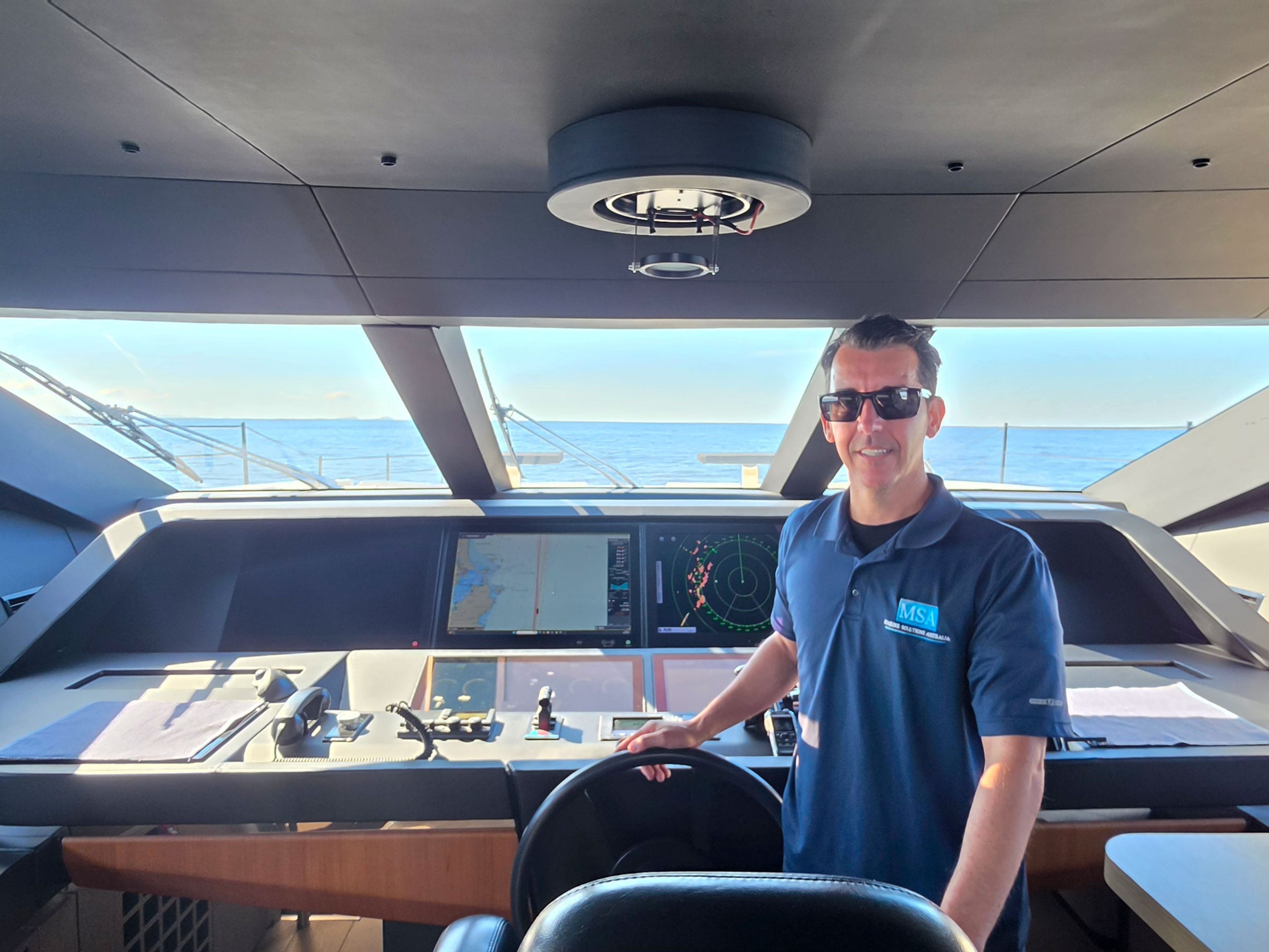 Marine Solutions delivery skipper at the wheel of a motor yacht with open water astern