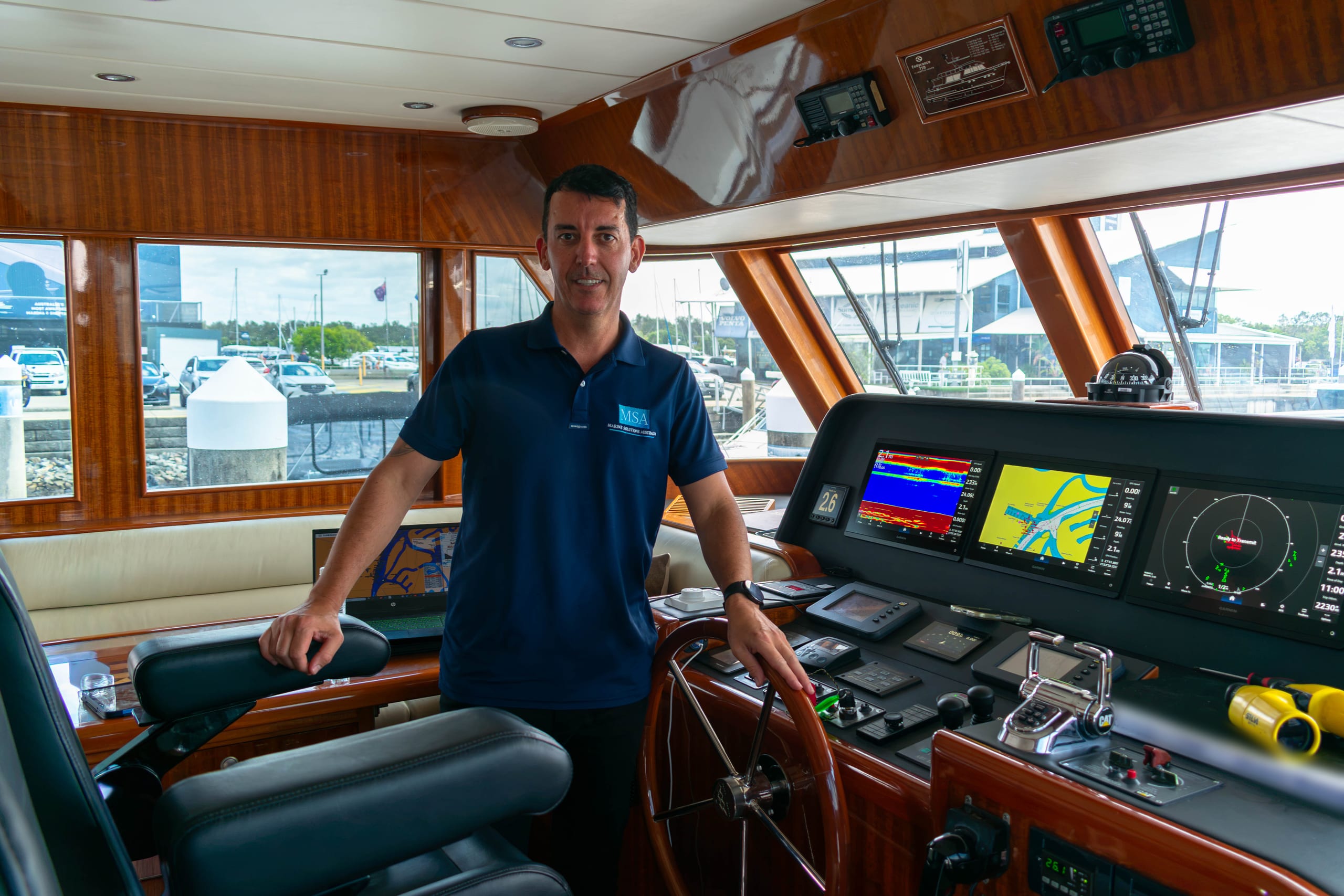 Marine Solutions Australia delivery skipper at the helm of a motor yacht berthed in a marina, navigation displays on