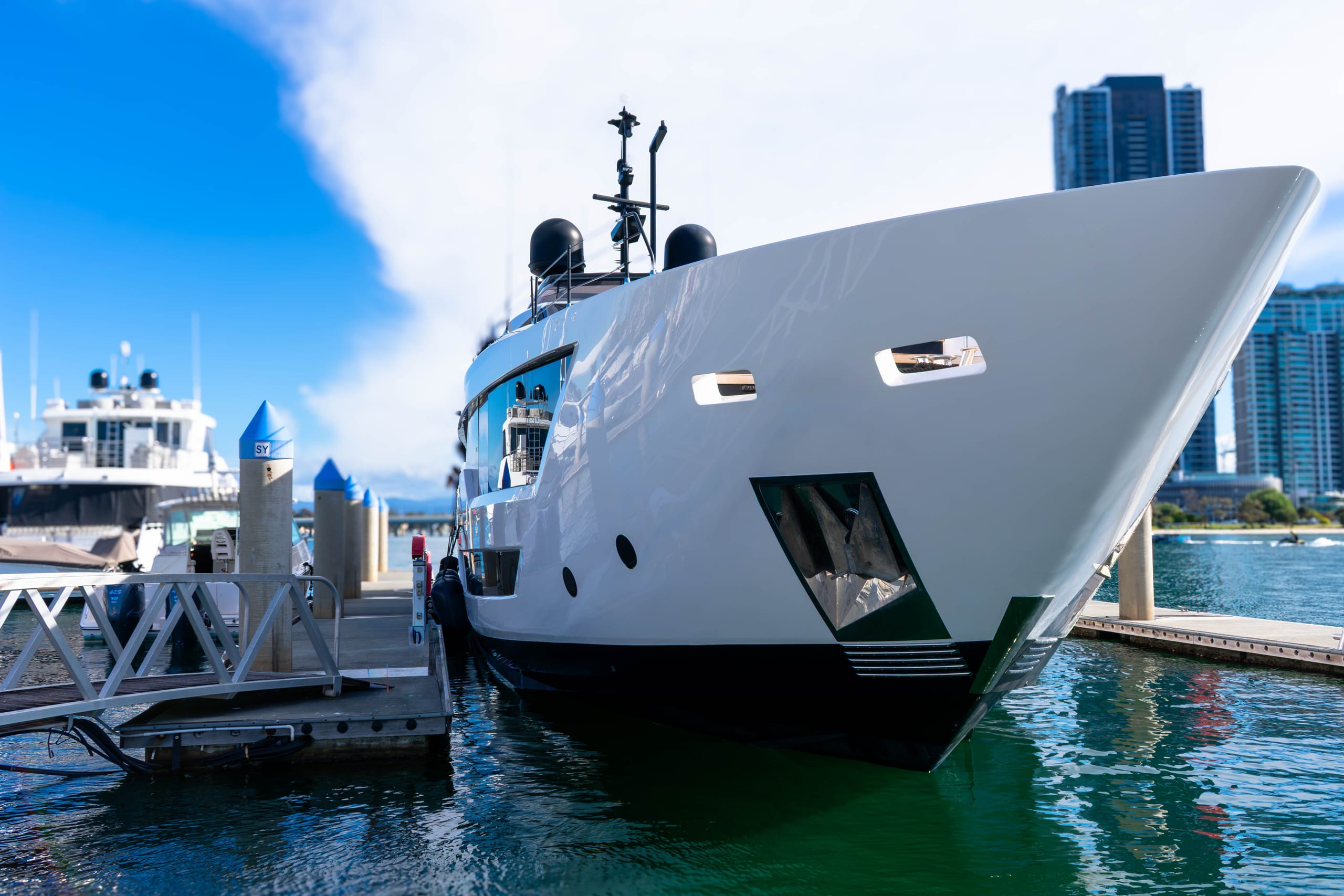 Superyacht bow secured in a tight marina berth between piles, city towers behind