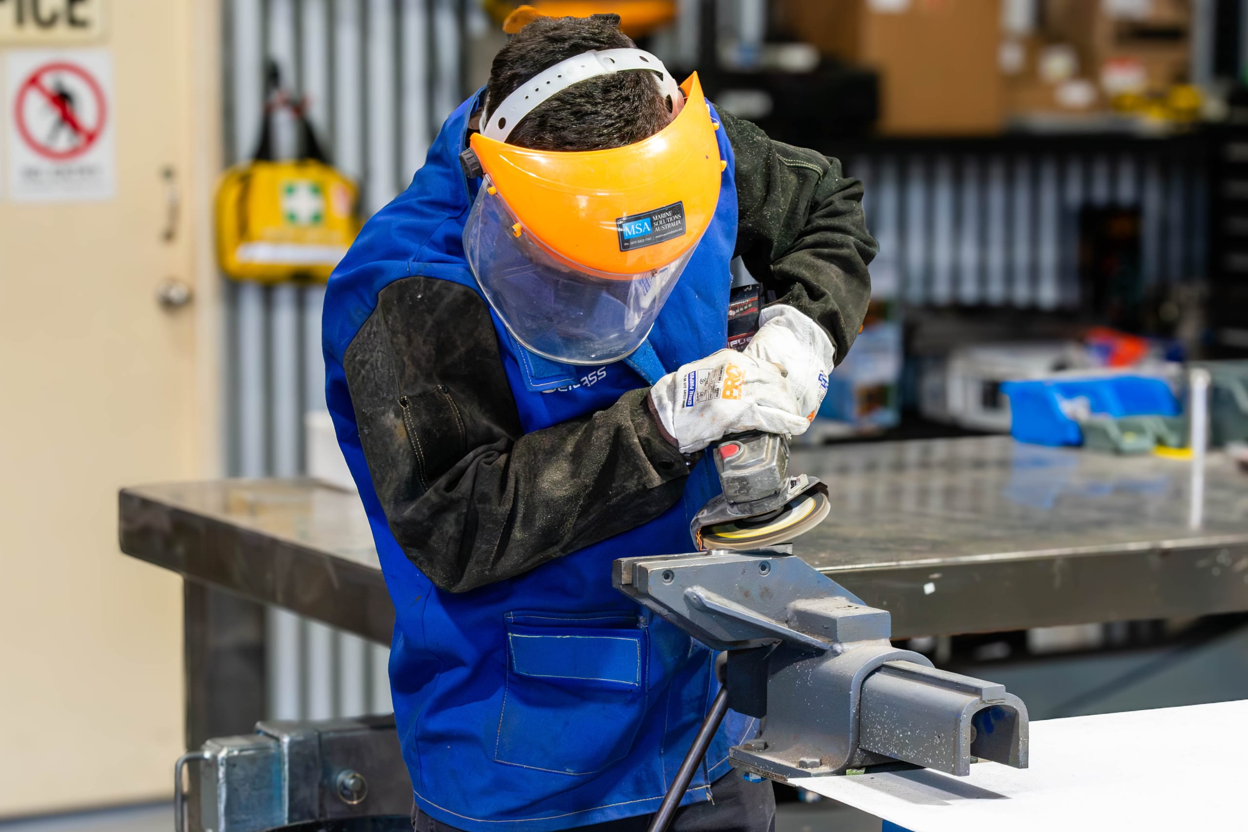Marine Solutions Australia technician in a face shield finishing a stainless steel part with a flap disc in a bench vice