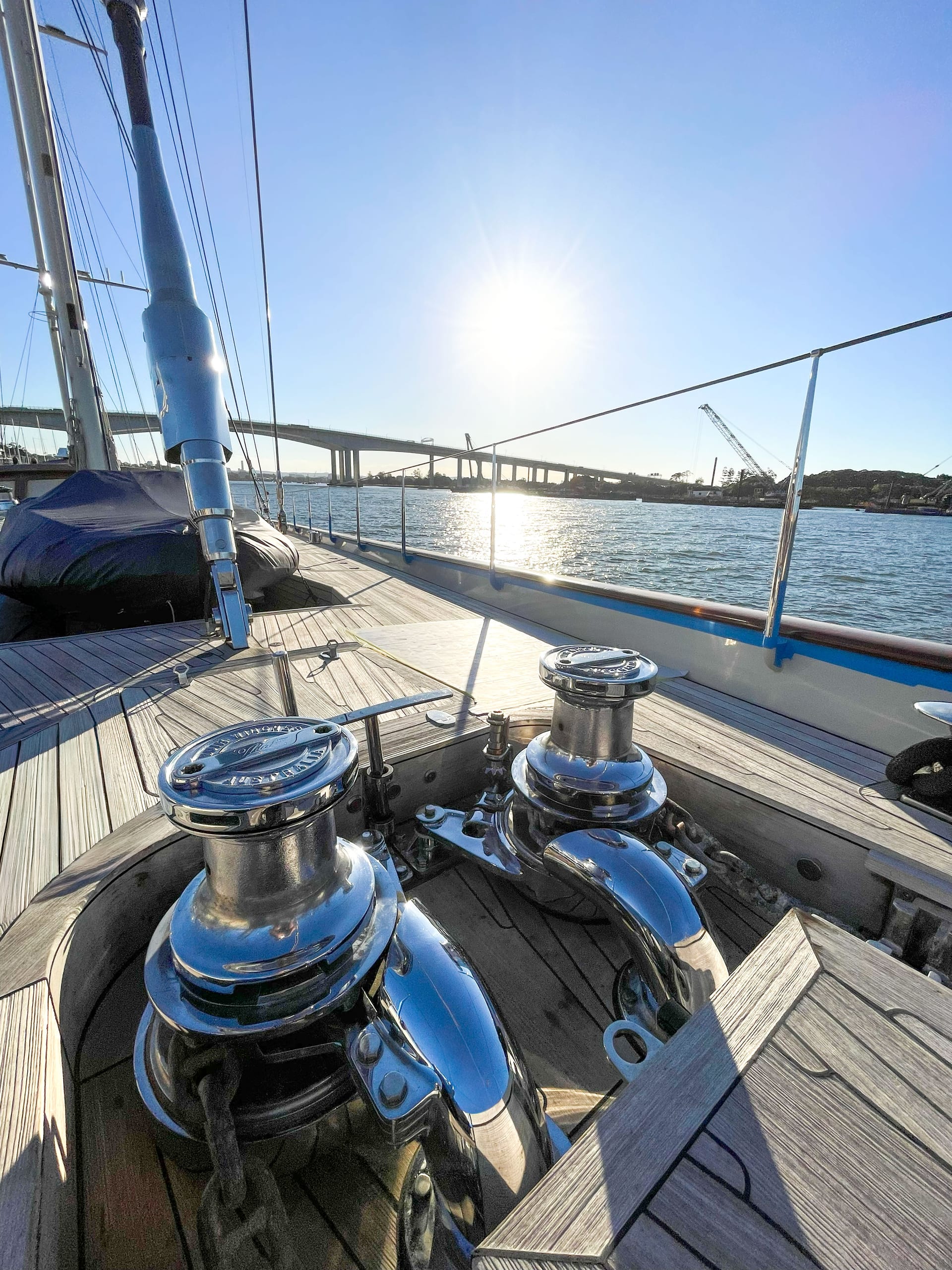Two new Muir windlasses on a teak foredeck looking aft along the sailing yacht, river and bridge behind