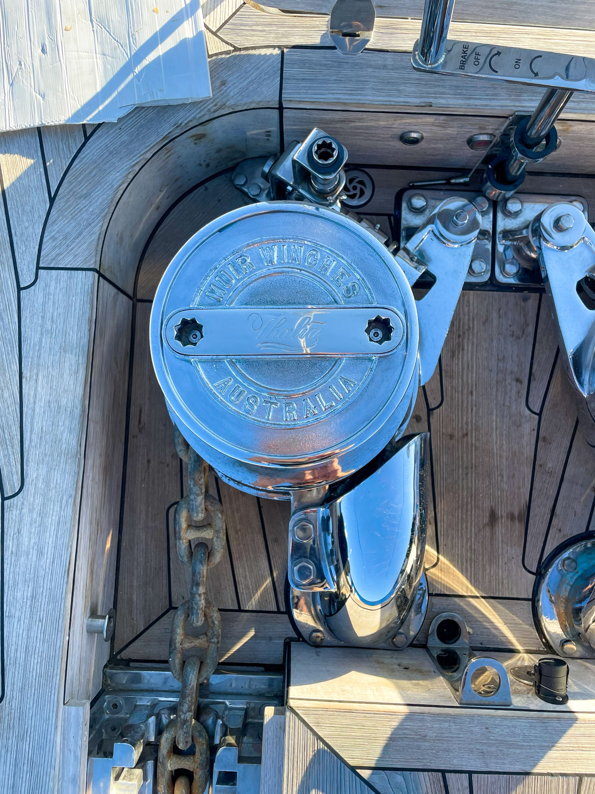 Close-up of a polished Muir windlass capstan and chain pipe fitted through a teak deck, anchor chain in the gypsy