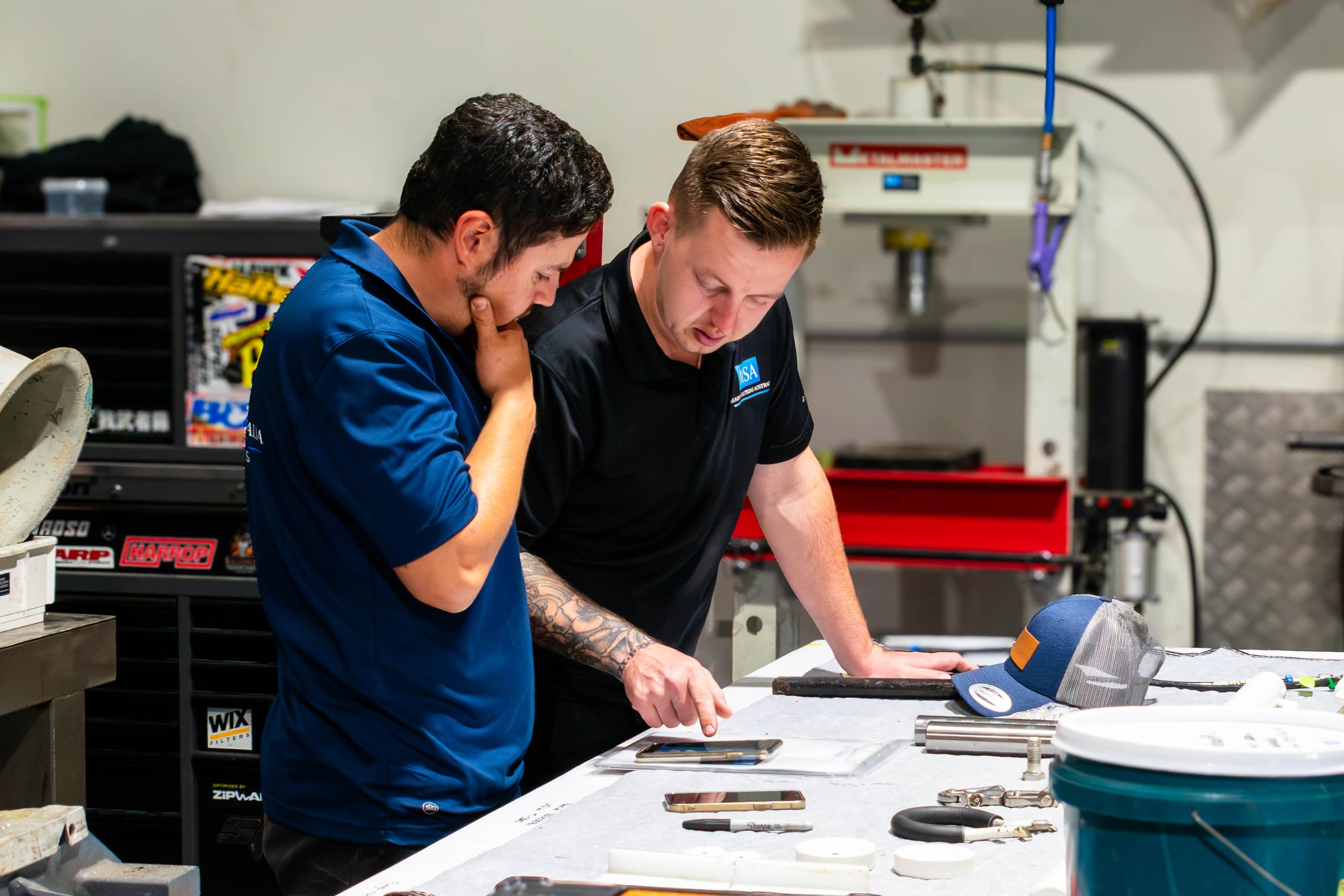 Two Marine Solutions Australia technicians reviewing job photos at the Coomera workshop bench