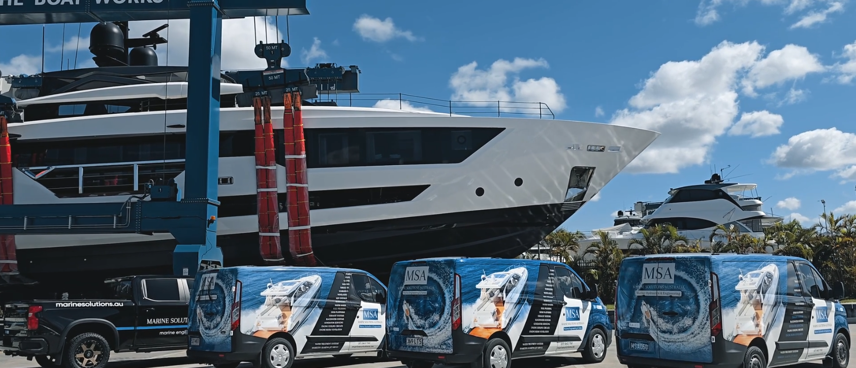 A superyacht in The Boat Works travel lift with Marine Solutions' service vans lined up in front